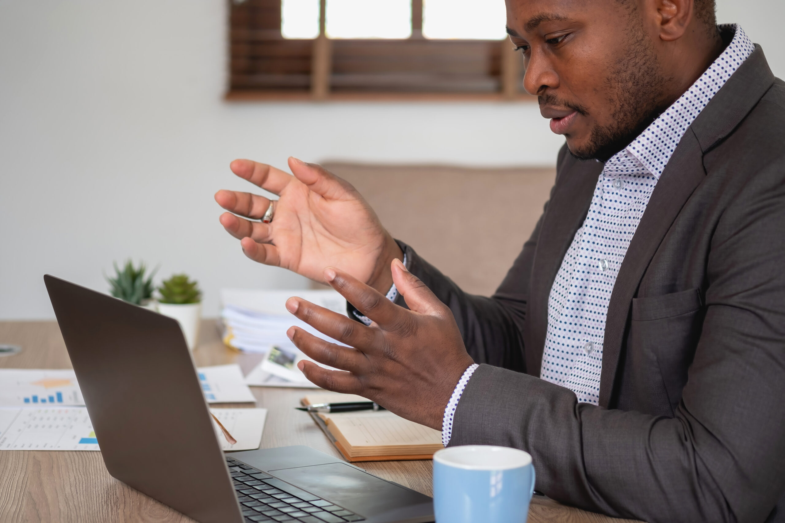African American businessman analyzing laptop graph paperwork in office holding documents preparing portfolio analysis report Black male analyst doing paperwork in the workplace using the computer.